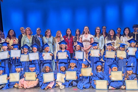 Together to Kindergarten graduates pose in caps and gowns with diplomas. Teachers, LICM Staff and elected officials stand behind them.
