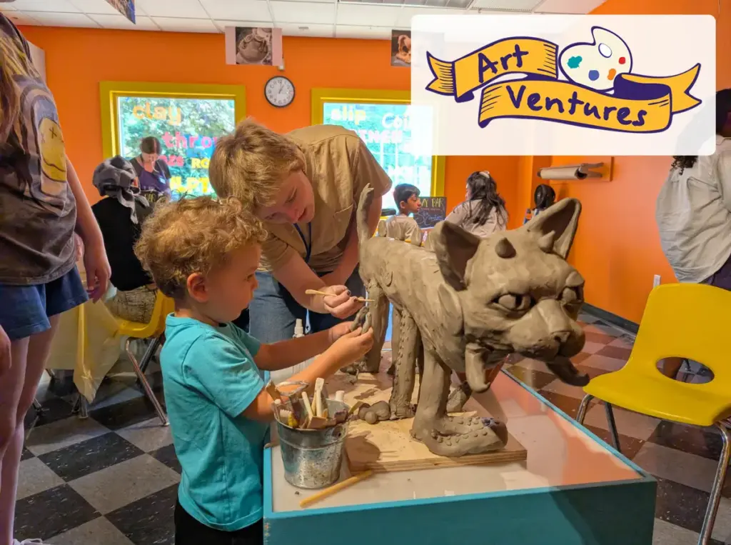 Museum intern and child in blue shirt work together on a clay sculpture