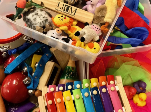 A bin of musical instruments and stuffed animals, including a tambourine printed with the LICM logo.