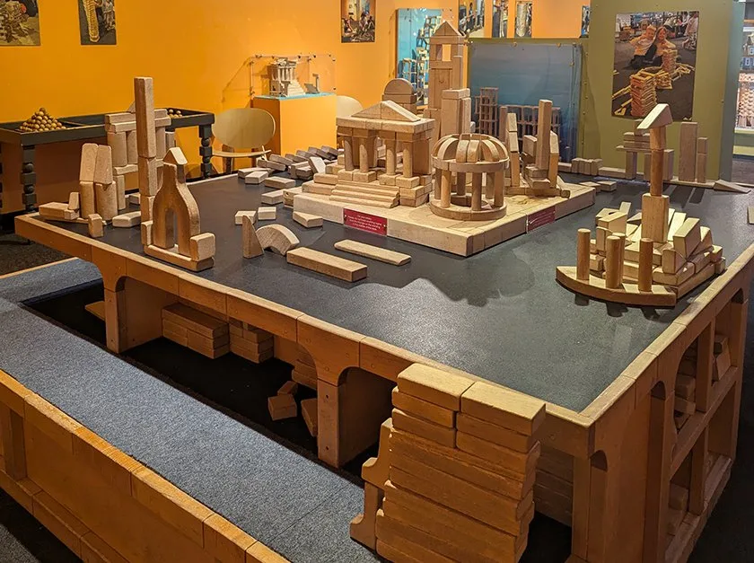 A large wooden square table with a black top, filled with various wooden blocks.