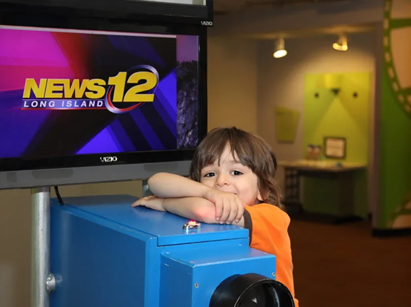 A child leaning on the News12 wooden camera.
