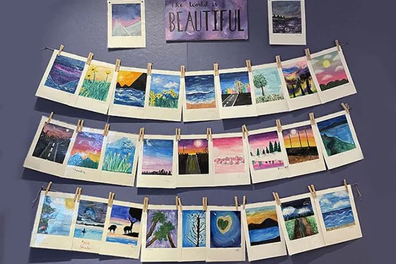 Students' artwork hung with clothespins on a purple wall.