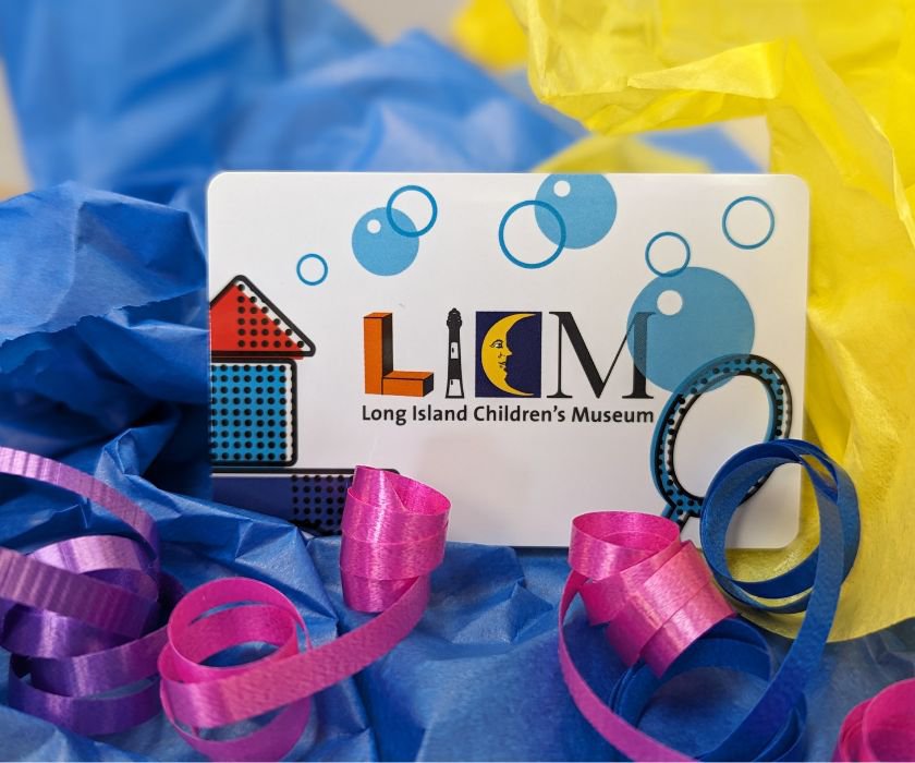 A white gift card with LICM logo, stacked colorful blocks and blue bubbles against a multi-colored tissue paper background.
