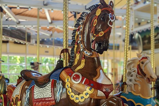 Close-up of a dark brown carousel horse decorated with bells and armor.