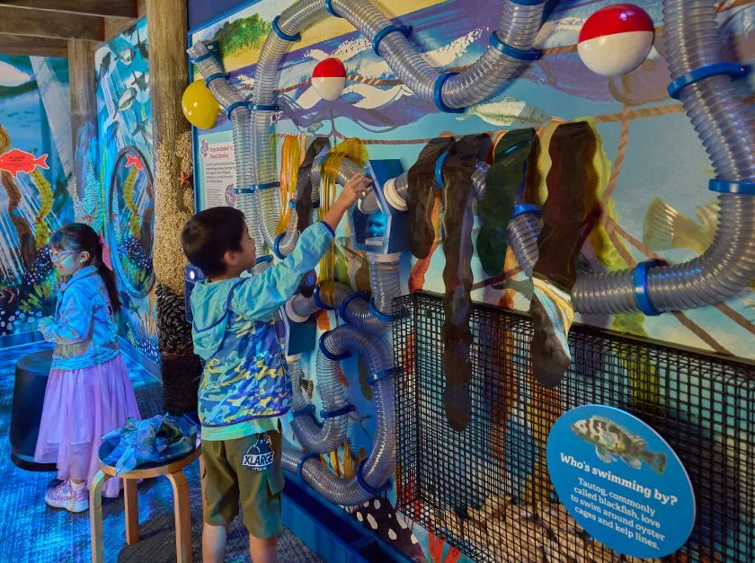 Children standing before colorful wall with underwater images and clear air tubes.