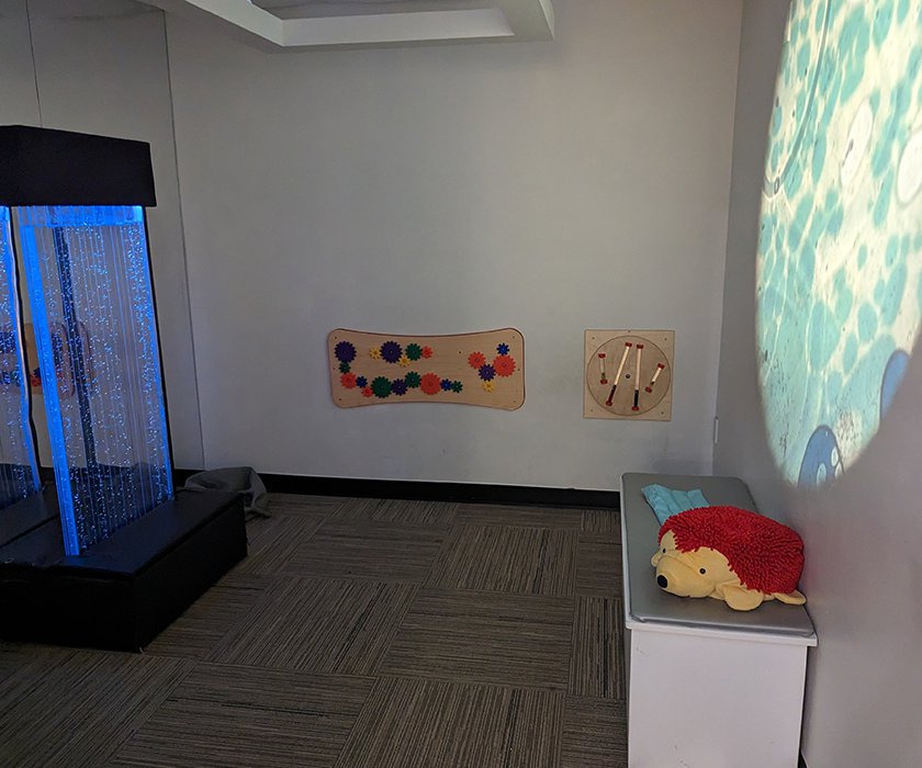 A calming sensory room with a bubble tower light feature, tactile wall panels, and a projected ocean scene.