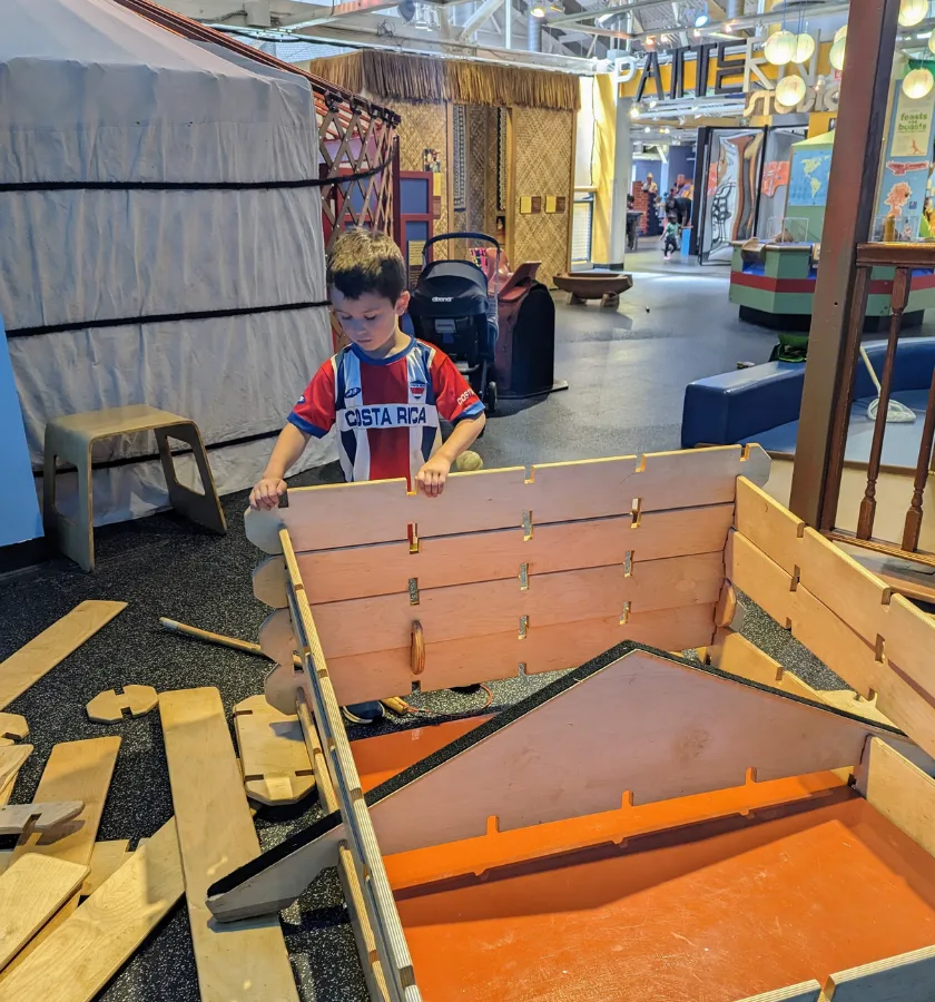 A child building a house with large wood planks.