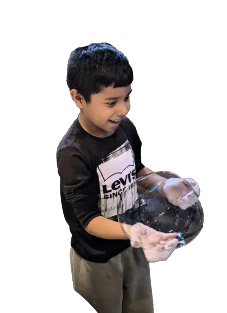 A boy smiles while holding a large bubble, shown on a plain background.