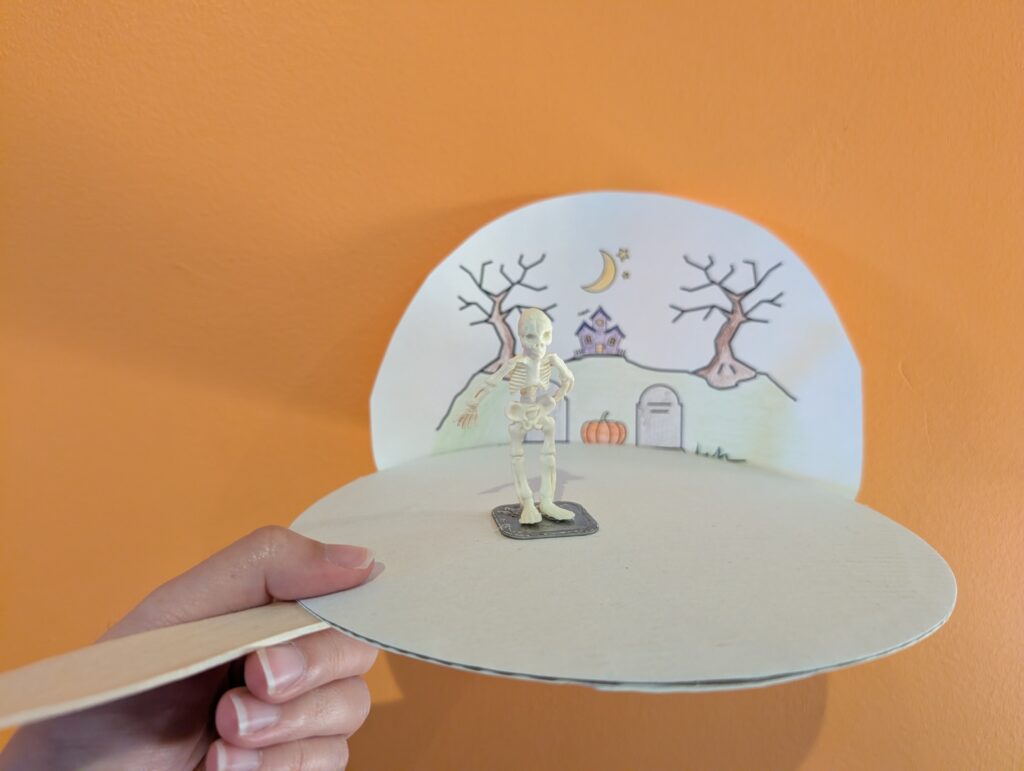 Paper drawing with a small plastic skeleton on a magnet. The magnet moves using the stick on the left of the picture.