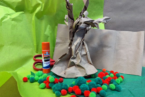 Paper mache tree with felt apples in front of green paper with glue stick.