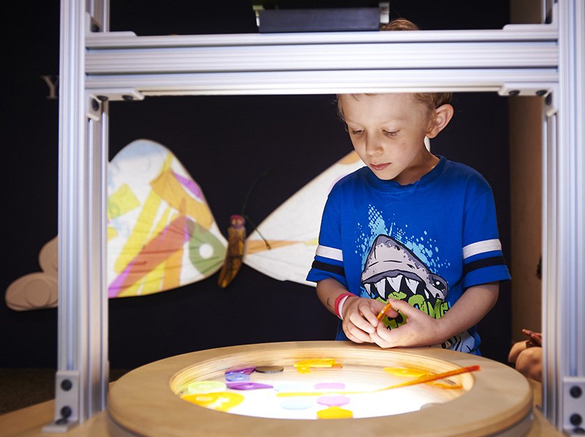 A child looking into a light box with a glowing butterfly in the background.