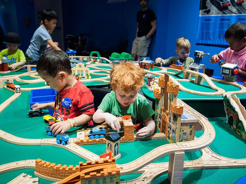 Children playing with trains at table of train tracks in Thomas exhibit.